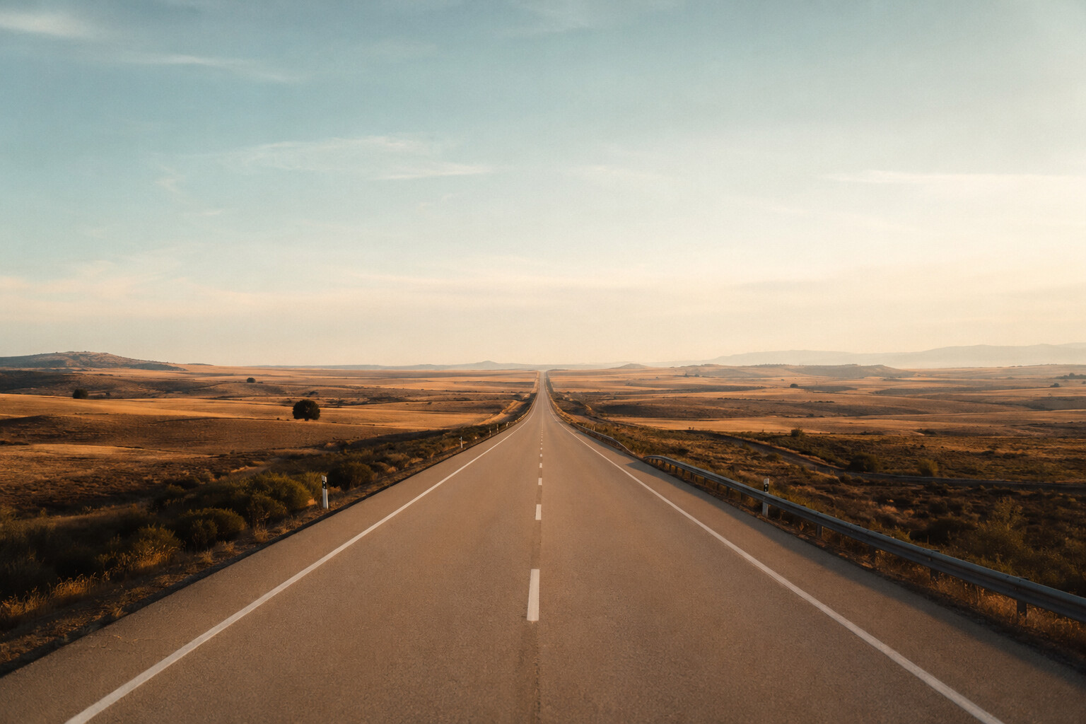 Kerzengerade leere Autobahn durch weite goldbraune Landschaft bis zum Horizont