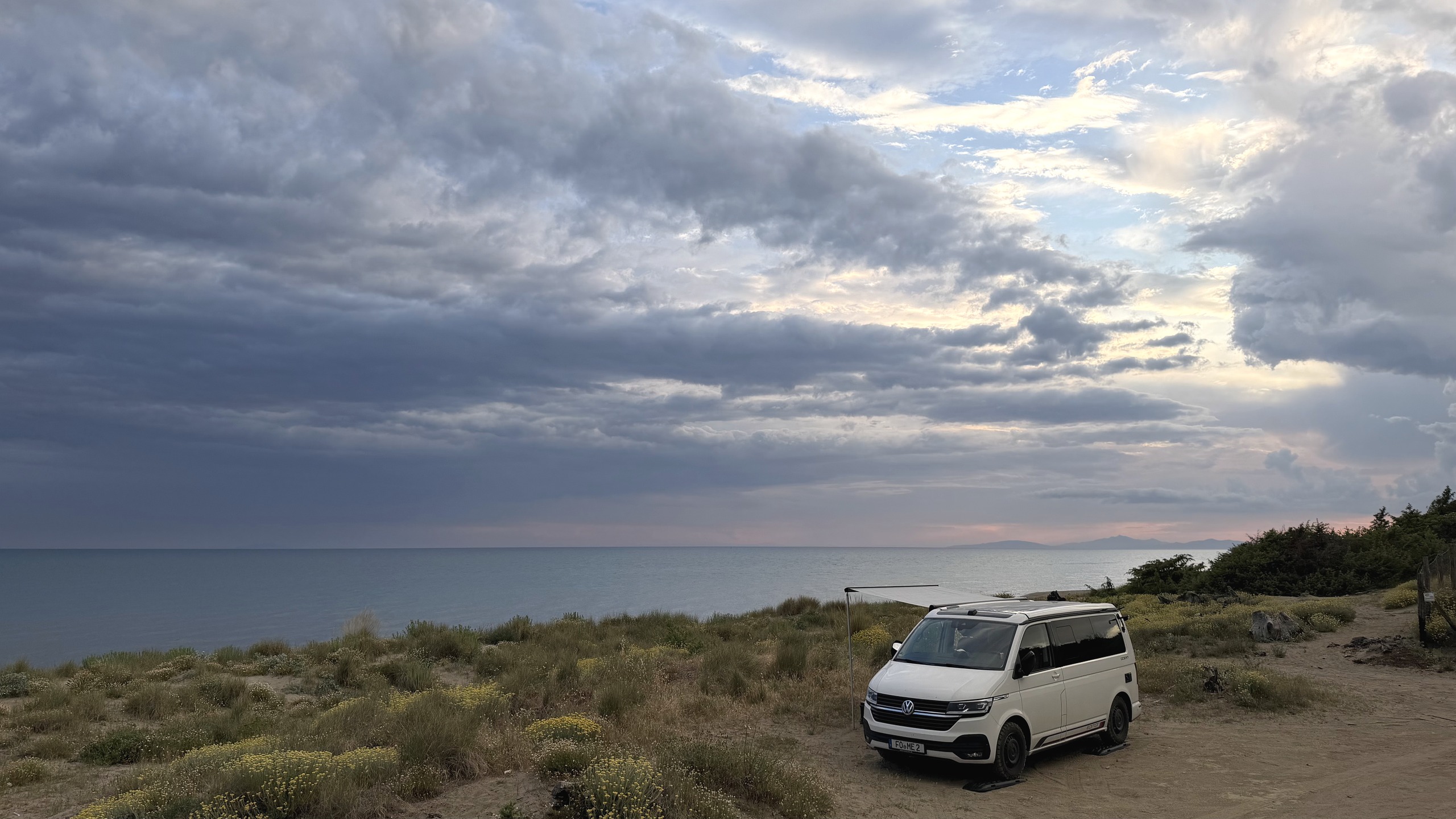Weißer VW-Campingbus Herbie steht bei Dämmerung frei am Meer