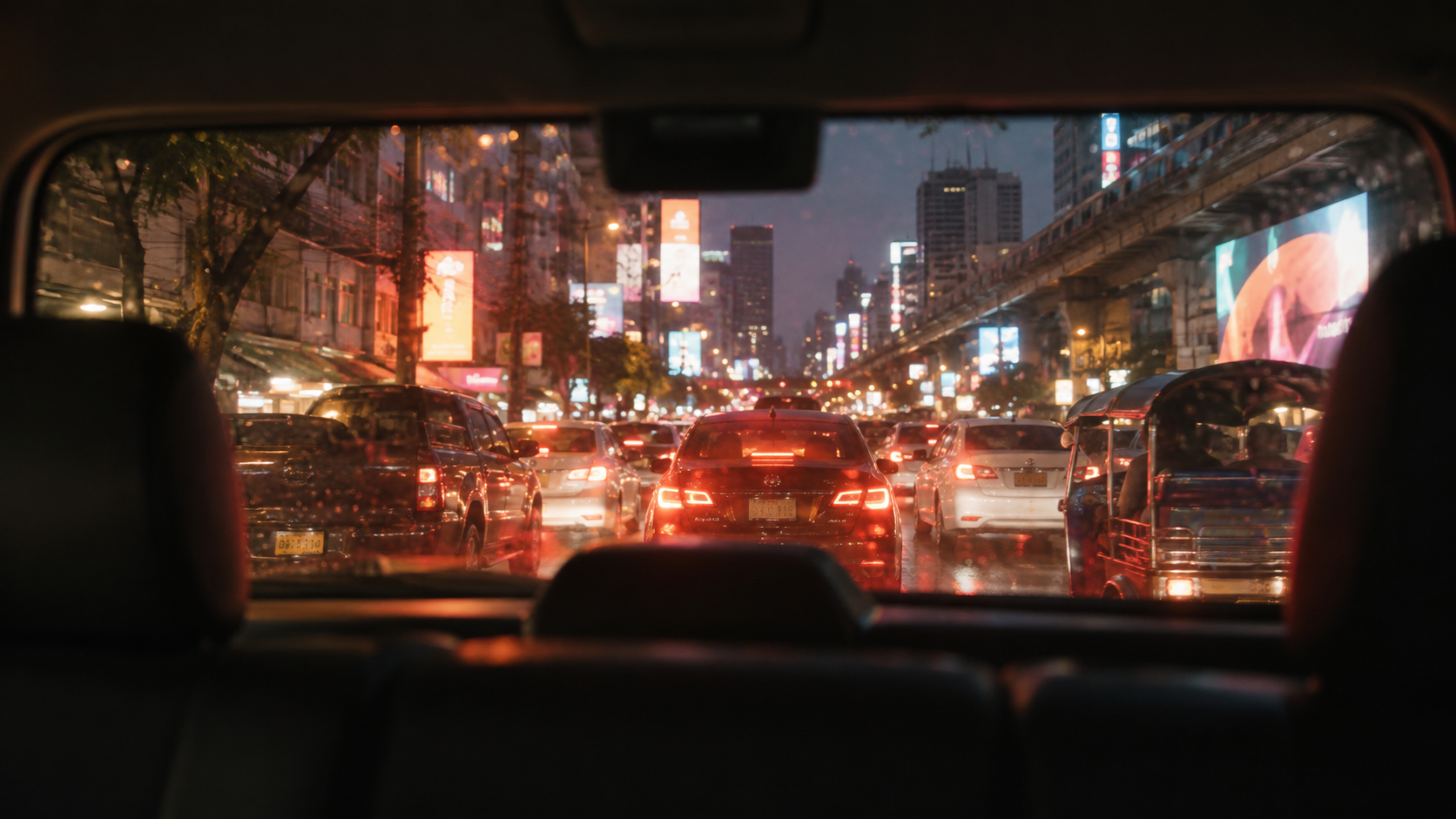 Blick aus einem Taxi auf den Bangkoker Abendverkehr mit Rücklichtern und Leuchtreklamen im Regen