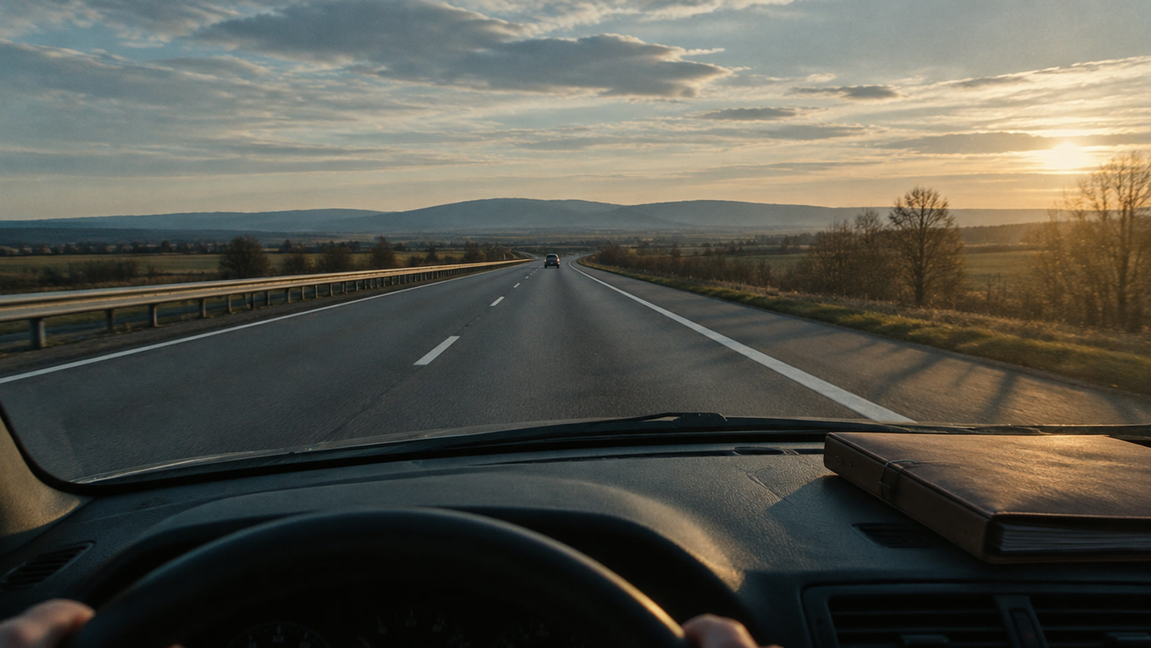 Blick durch die Windschutzscheibe auf eine fast leere Autobahn im Nachmittagslicht, auf dem Armaturenbrett ein Aktenordner.